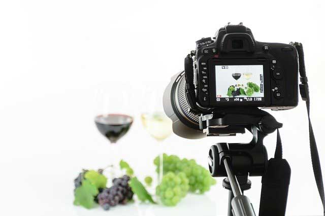 A camera taking a picture of wine and grapes in a studio.